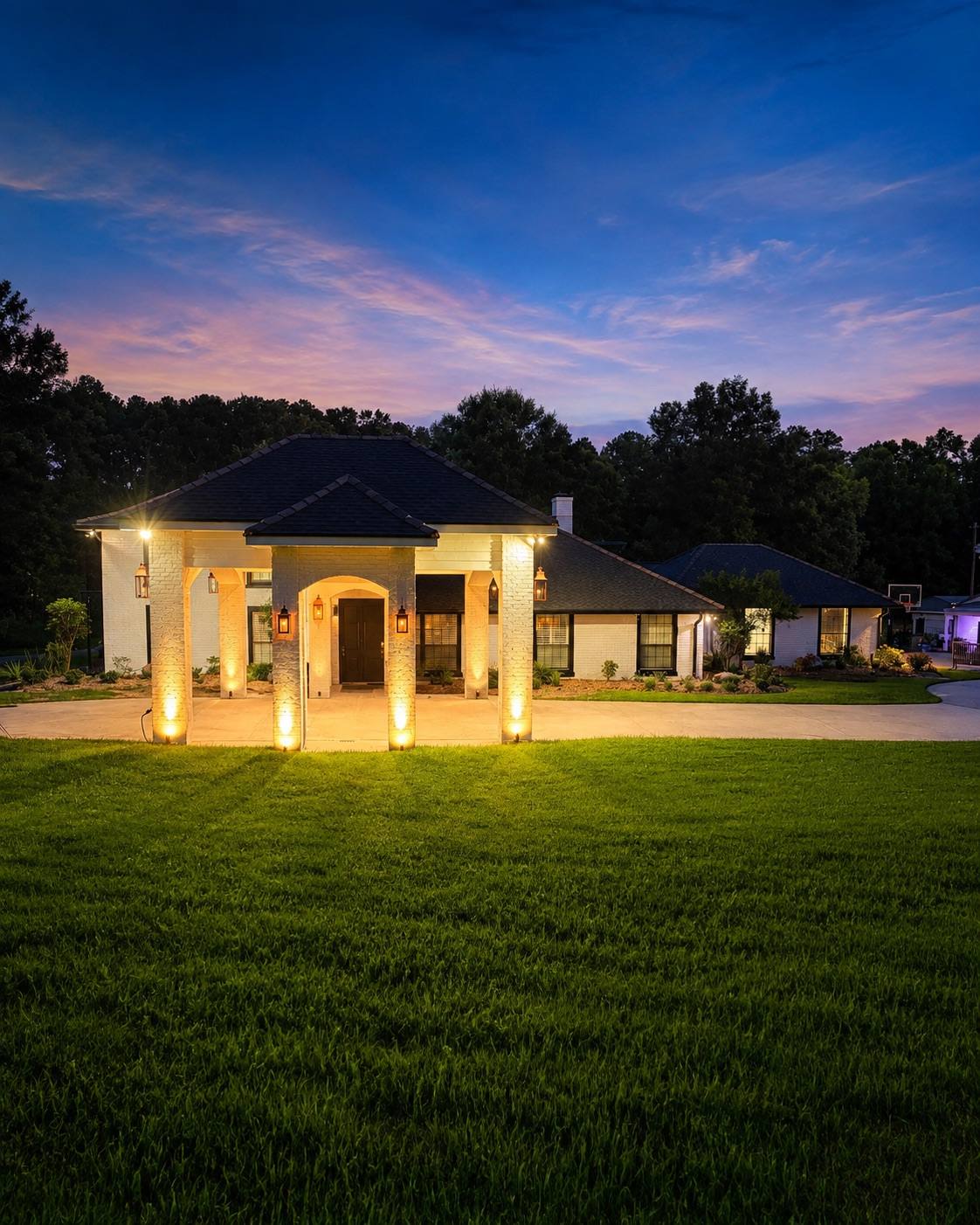 Custom home at twilight under a pink and blue sunset, the columned entry and landscape lighting lit against a manicured lawn
