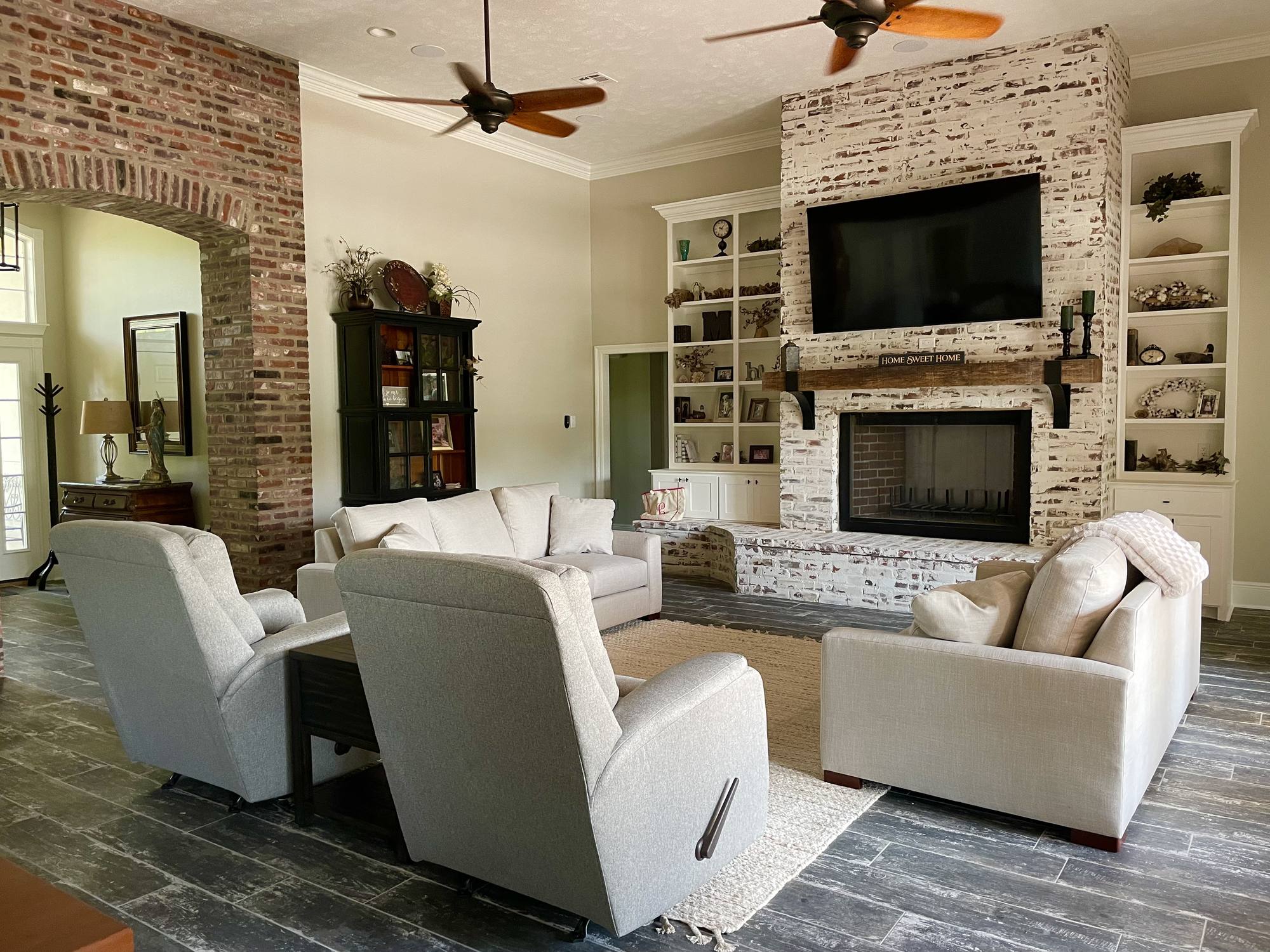 Finished living room with a whitewashed brick fireplace, reclaimed beam mantel and painted built-in shelving on both sides