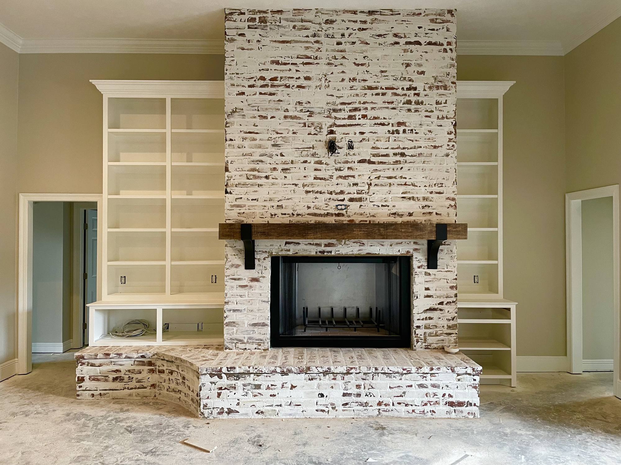 Whitewashed brick fireplace with a rough-sawn beam mantel flanked by symmetrical white built-in bookcases